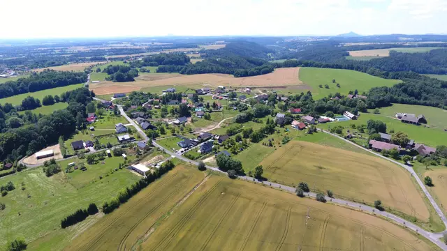 Jivina obklopená poli a lesy, na obzoru kuželovitý kopec