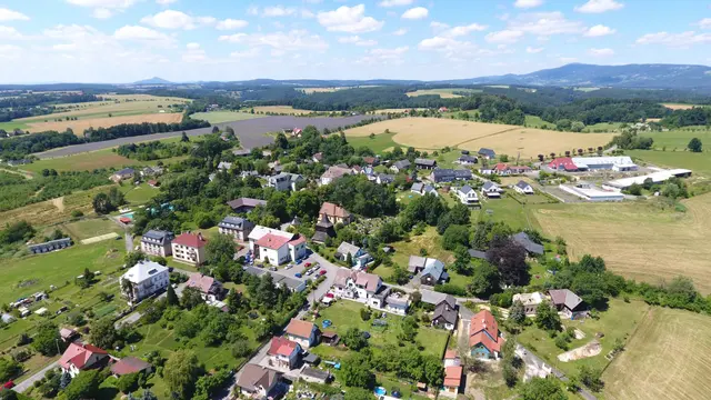 Střed Vlastibořic s bytovými domy, vzadu zemědělský areál a kuželovitý kopec
