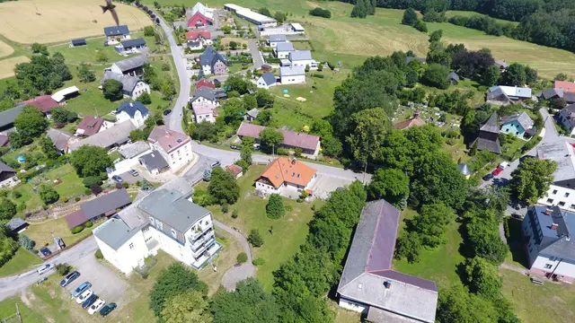 Střed Vlastibořic zblízka: bytový dům s balkony, dřevěná zvonice a dlouhá budova