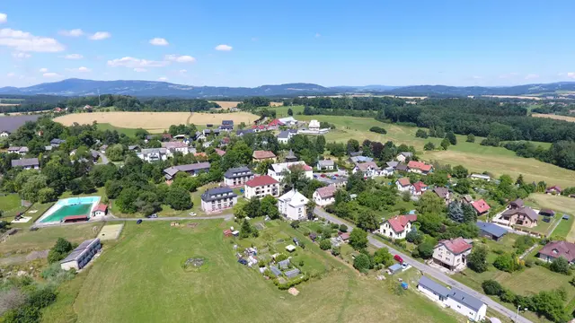 Vlastibořice z dronu: zástavba podél silnice, vlevo vodní nádrž, v pozadí hřebeny hor