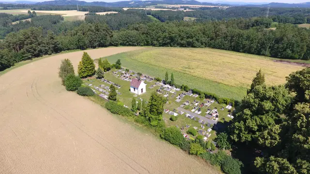Hřbitov s bílou kaplí mezi poli a lesem, pohled z dronu