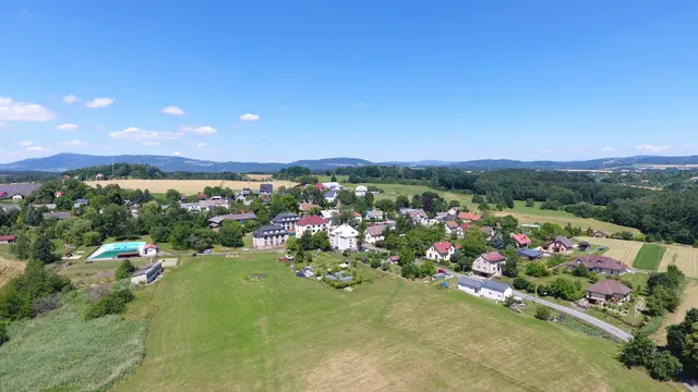 Vlastibořice z dronu: bytové domy, vodní nádrž a domy podél silnice, v pozadí hory